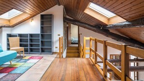 A loft bedroom with a sloped ceiling, wooden beams, a skylight, a built-in bookshelf, a colorful rug, and a staircase. - Casa Tranquillità Lario, Plesio, Italy (Plesio)