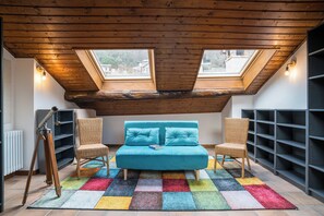Ein Schlafzimmer im Loft-Stil mit einem türkisblauen Sofa, zwei Sesseln, einem farbenfrohen Teppich und Dachfenstern.