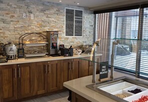 A breakfast bar with a stone wall backdrop, a coffee machine, and a glass display case with food items. - Accessible King Studio w/ Sofa Bed + Kitchen (Vaughan)