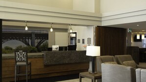 Een hotel lobby met een receptiebalie, zithoek en een groot raam met uitzicht op een brug.