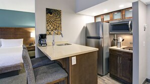 Een compacte hotelkamer met kitchenette, een bed, een klein zithoekje en een decoratief wandobject.
