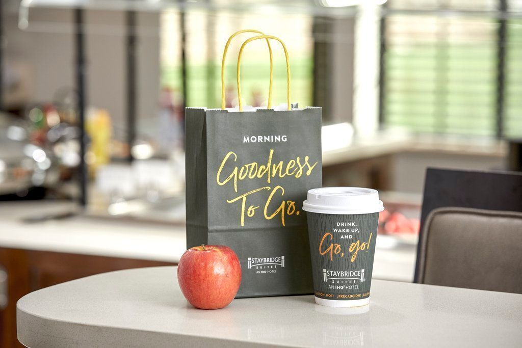 Une tasse de café et un sac noir sur lequel on peut lire « Goodness to Go » sont posés sur une table.