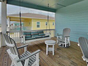 A covered porch with a swing, Adirondack chairs, and a small table. - Pelican's Landing (Rockport)