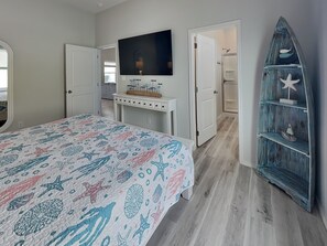 A bedroom with a bed, a TV, a dresser, and a decorative shelf. - Pelican's Landing (Rockport)