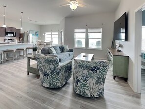 A modern living room with a sofa, two armchairs, a dining table, and a kitchen area with bar stools. - Pelican's Landing (Rockport)
