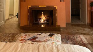 A room with a fireplace, a bed with a floral bedspread, a ceiling fan, and a painting above the fireplace. - 🌿 A Hidden Paradise Between Nice and Villefranche (Nice)