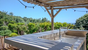 Un área de bar al aire libre con una pérgola, luces colgantes y vistas a un viñedo.