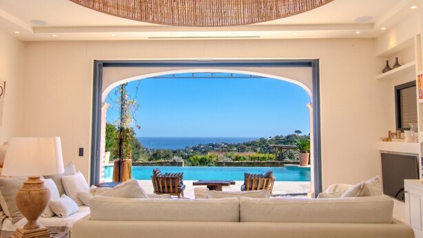 Un salón con un amplio ventanal de arco, una piscina y vista al mar.