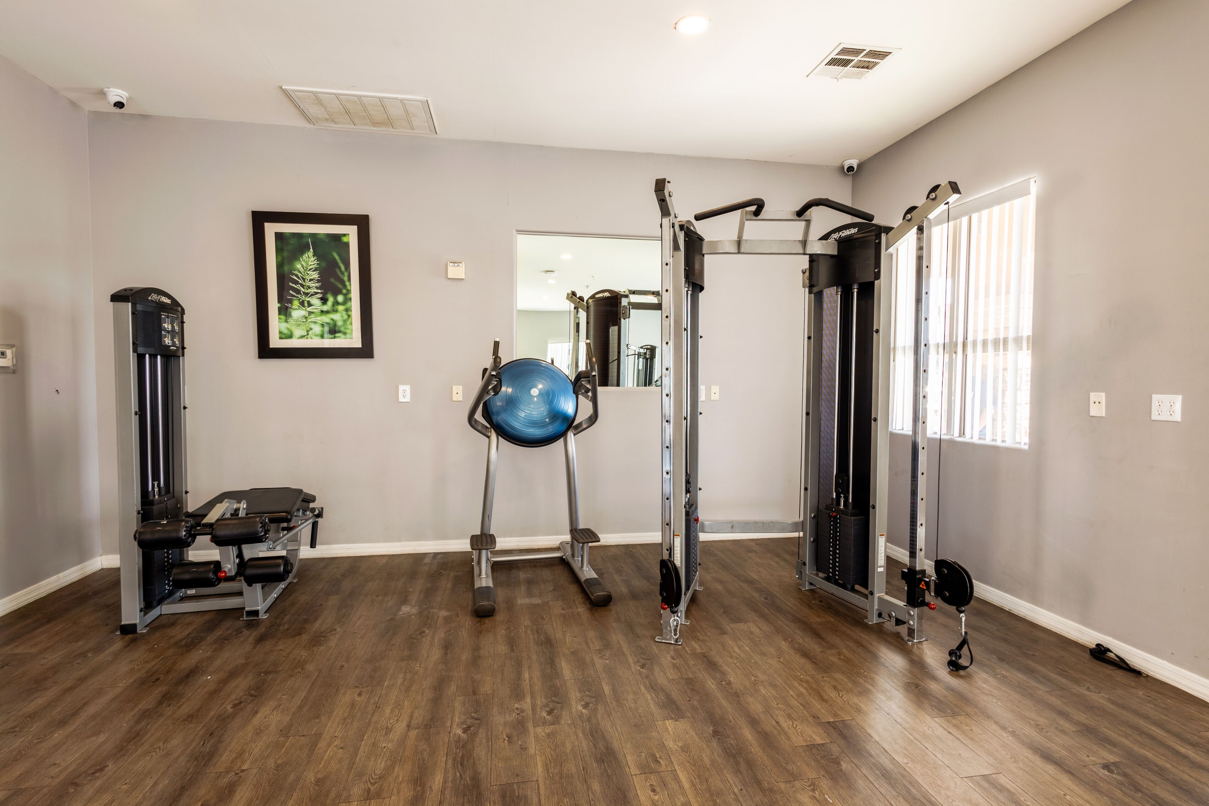 A gym with exercise equipment, a framed picture on the wall, and a window with blinds.