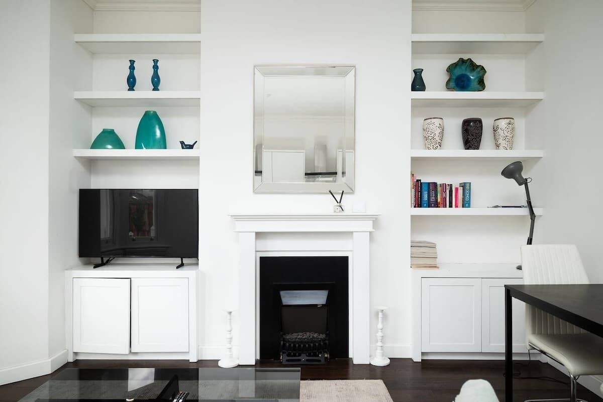 Una sala de estar con chimenea, estanterías blancas con adornos, un televisor de pantalla plana y una mesa de centro.