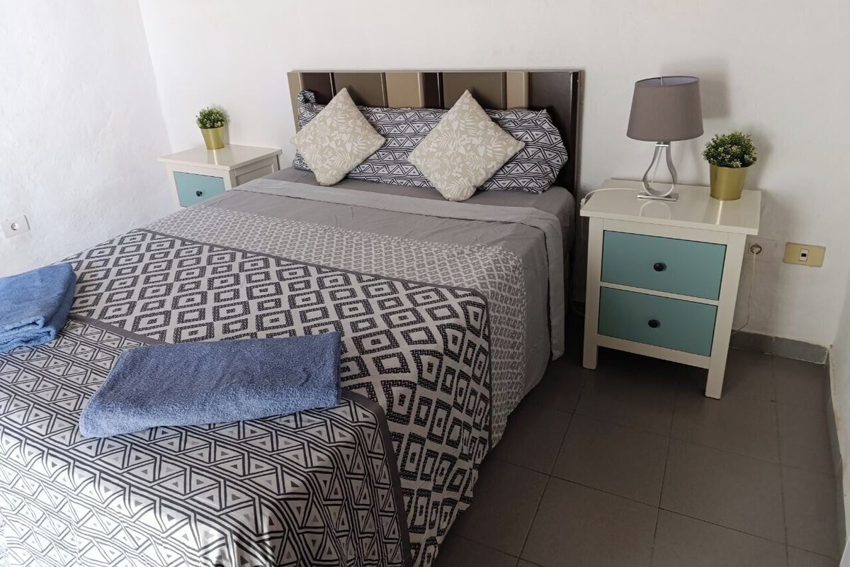 A bedroom with a bed, two nightstands, a lamp, and a potted plant.