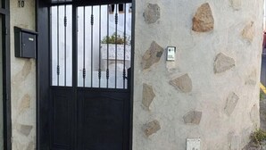 Un bâtiment en pierre avec un portail en métal noir, un petit marchepied menant à l’entrée et une boîte aux lettres fixée au mur.