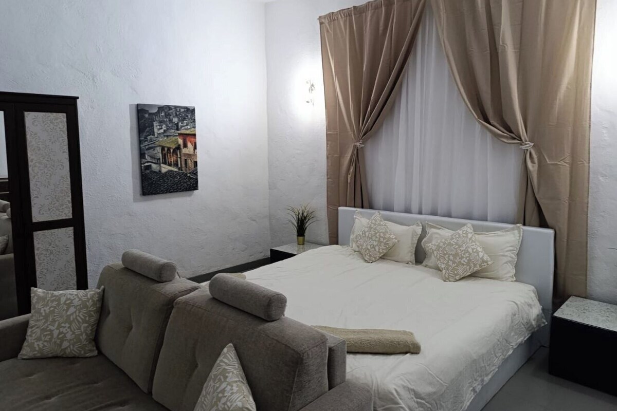 A bedroom with a bed, a nightstand, a chair, a wall-mounted plant, and a painting.