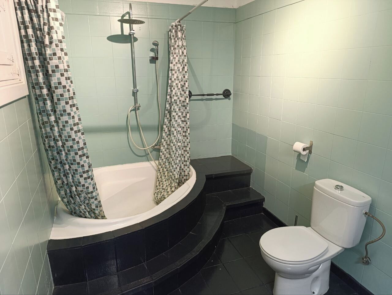 Une salle de bain avec une baignoire, une douche, des toilettes et des murs carrelés.