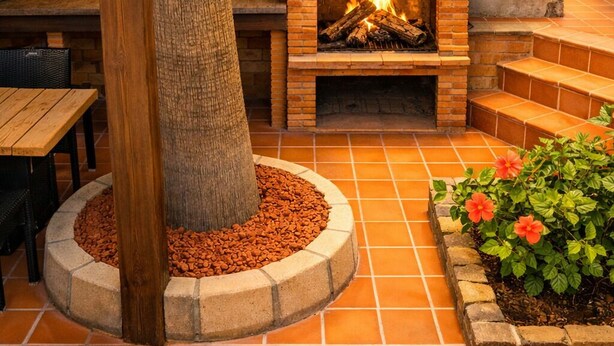 Une terrasse extérieure avec une cheminée en pierre, une table en bois et un arbre.