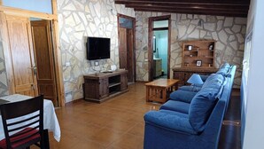 Un salon avec un canapé bleu, un meuble de rangement en bois, des murs décorés d’un motif imitant la pierre et un sol carrelé.