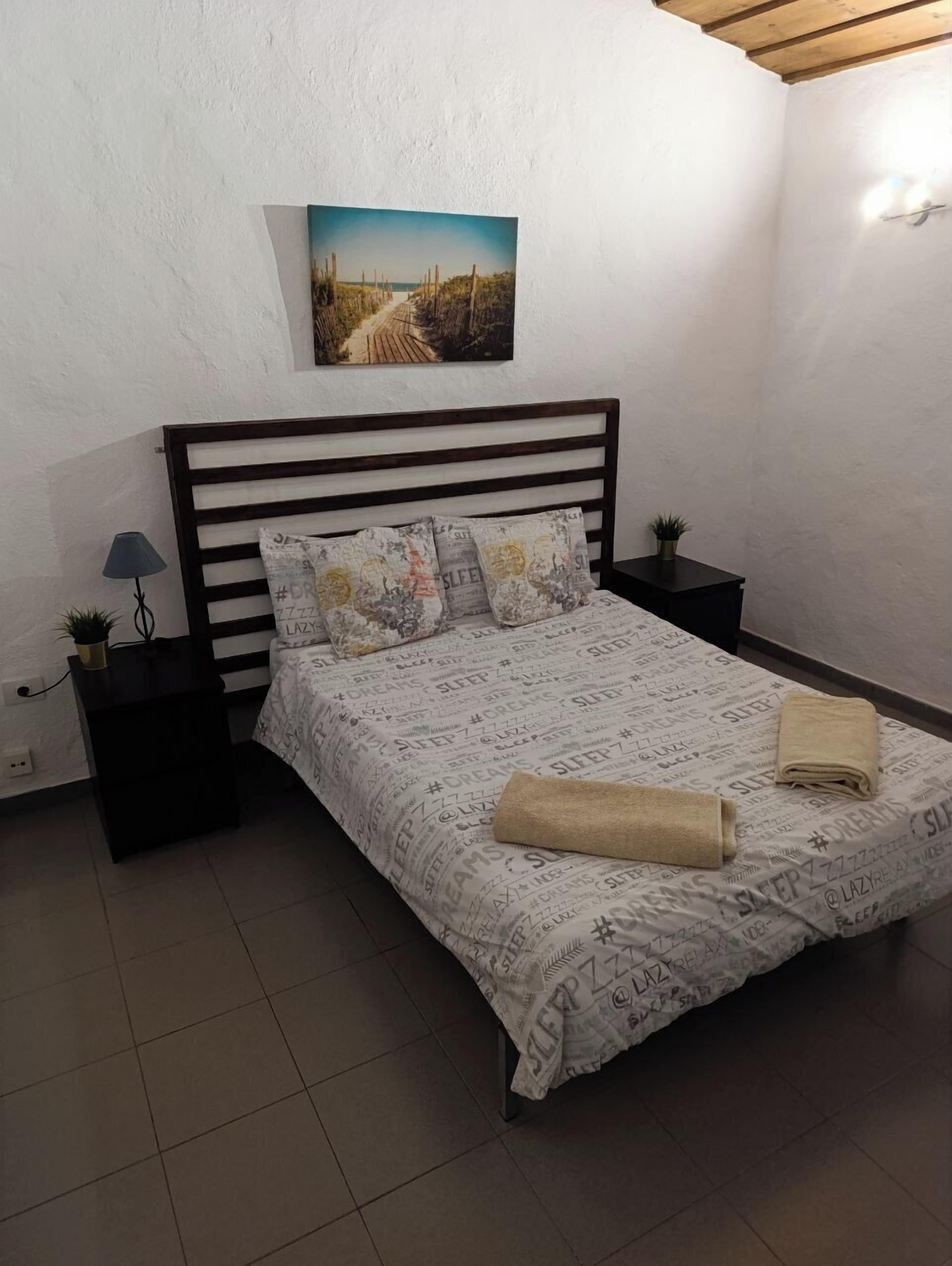 Une chambre à coucher avec un lit, deux tables de chevet, une lampe, un tableau et une serviette sur le lit.
