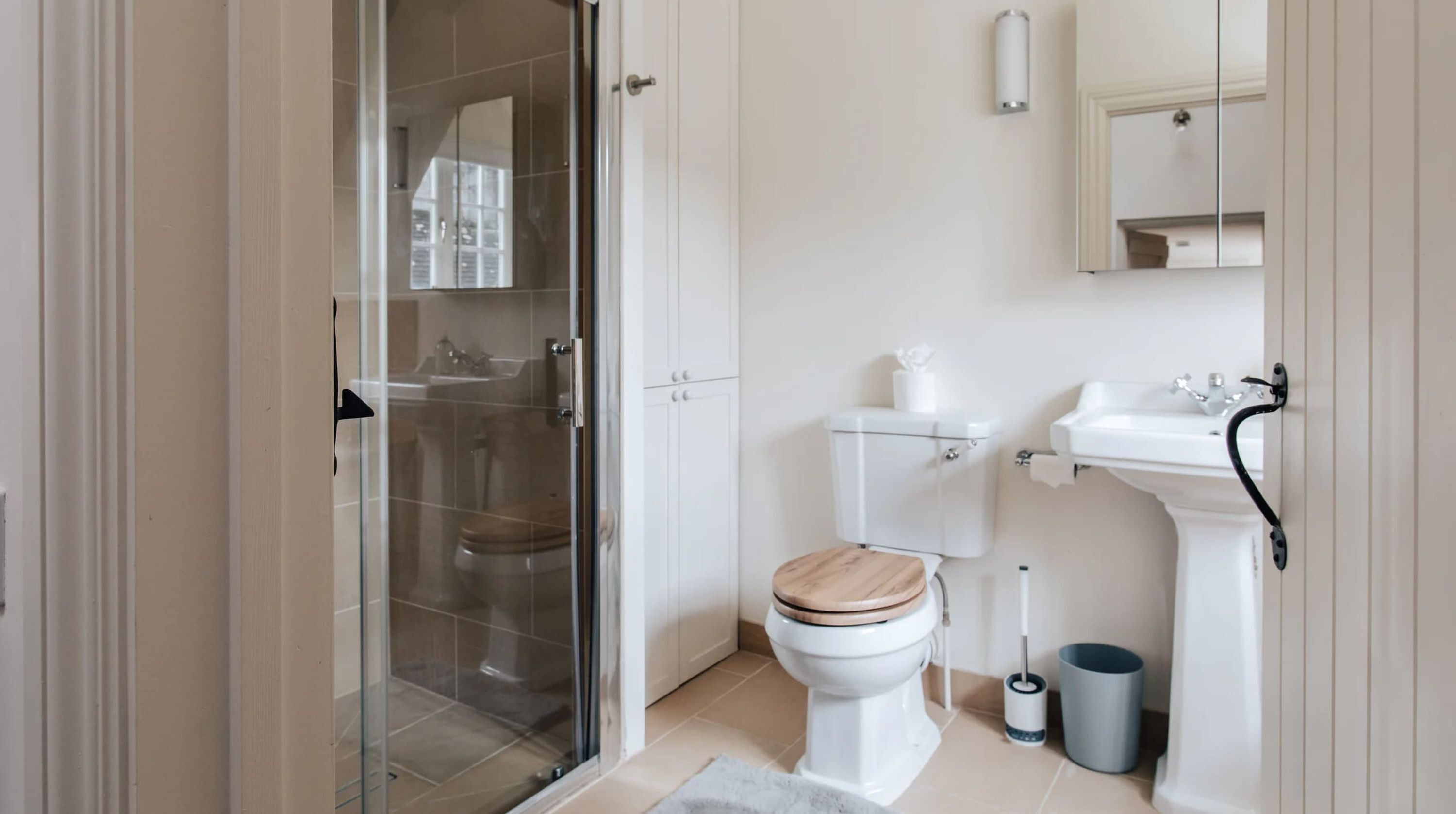 Une salle de bain avec une douche à parois de verre, des toilettes avec un abattant en bois, un lavabo blanc et un miroir au-dessus du lavabo.