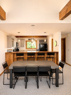 A modern kitchen with a large island, wooden cabinets, and a dining area with a long table and chairs.