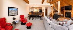 A modern living room with a gray sofa, red chairs, a dining area with a kitchen in the background, and a fireplace.