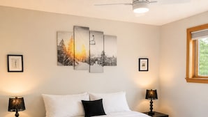 A bedroom with a bed, two bedside tables, a ceiling fan, and wall art. - Okemo Trailside: 3BR + Bonus Room, Hot Tub, Sauna & On-Demand Shuttle to Sachem (Ludlow)