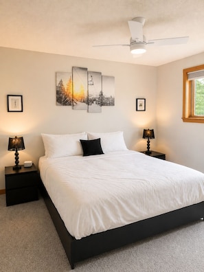 A bedroom with a bed, two bedside tables, a ceiling fan, and wall art.