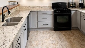 A kitchen with white cabinets, a black stove, a microwave, and a coffee maker. - Okemo Trailside: 3BR + Bonus Room, Hot Tub, Sauna & On-Demand Shuttle to Sachem (Ludlow)