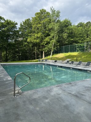 Una piscina con una escalera de metal, rodeada de césped y árboles.