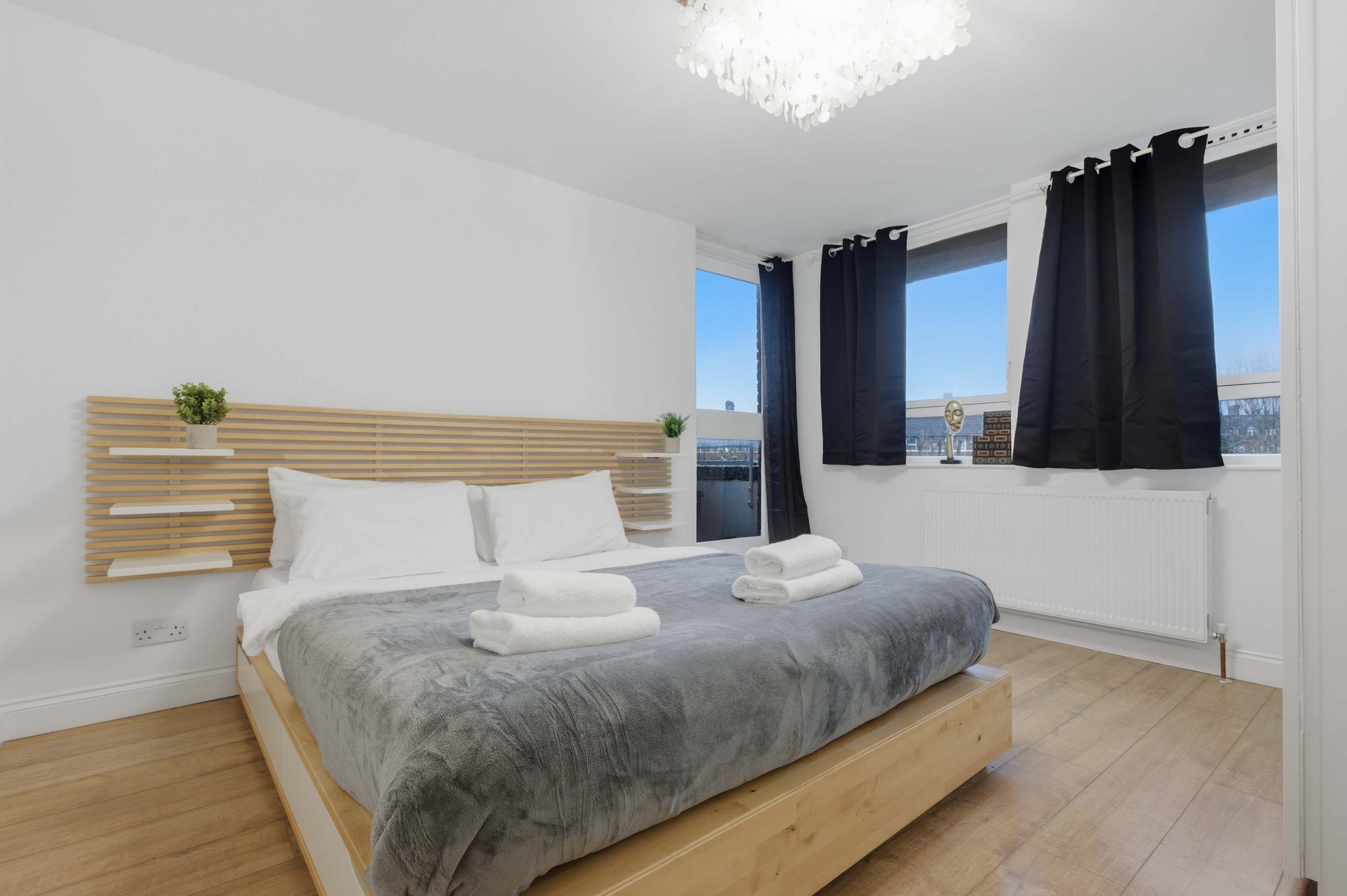 A modern bedroom with a bed, bedside tables, a view of the city, and a window with curtains.
