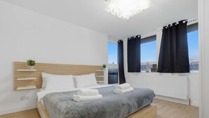 Een moderne slaapkamer met een bed, nachtkastjes, uitzicht op de stad en een raam met gordijnen.