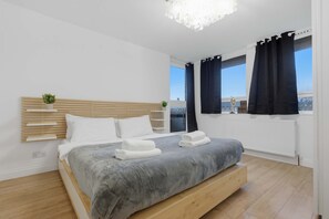 Une chambre moderne avec un lit, des tables de chevet, une vue sur la ville et une fenêtre avec des rideaux.