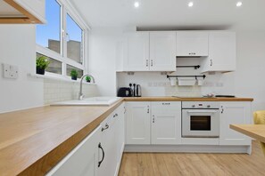 Une cuisine moderne avec des meubles blancs, un plan de travail en bois, un évier et un four.