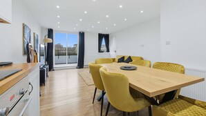 Een eetgedeelte met een houten tafel en gele stoelen, een keuken met moderne apparatuur, en uitzicht door grote ramen.