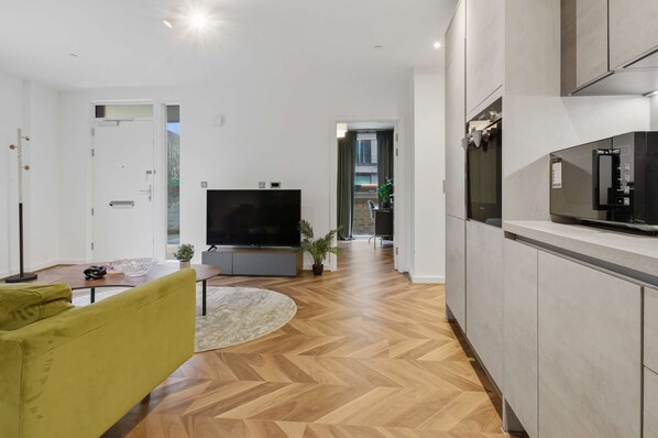 Ein modernes Wohnzimmer mit Flachbildfernseher, einer Couch, einem Couchtisch und einer Küchenzeile inklusive Schränken und Kühlschrank.
