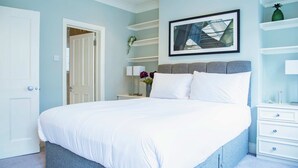 Ein Schlafzimmer mit einem Bett, einem Nachttisch, einem an der Wand befestigten Regal und einer Tür.