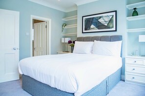 Une chambre à coucher comprenant un lit, une table de chevet, une étagère fixée au mur et une porte.