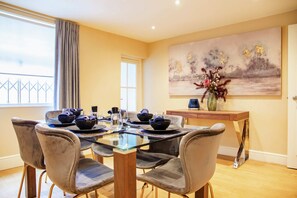 Un coin repas avec une table en verre, des chaises à revêtement gris, un vase avec des fleurs et un tableau accroché au mur.
