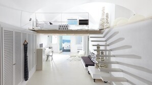Une chambre d’hôtel moderne, à aire ouverte, avec une mezzanine, un coin salon doté de coussins et une vue sur la mer.