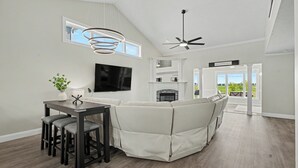 A modern living room with a sectional sofa, a dining table with chairs, a flat-screen TV, a fireplace, and a ceiling fan. - Luxury Lake & Golf Escape: 4BR & 4BTH Home + Gym,Near UIUC / U of I - Sleeps 11+ (Champaign)