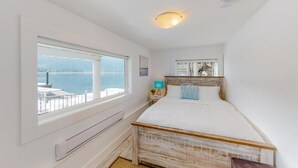 Een slaapkamer met een groot raam, een bed, een nachtkastje en uitzicht op zee.