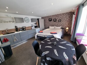 Une chambre moderne équipée d’une cuisine, d’un lit, d’une table à manger et d’un mur en briques.