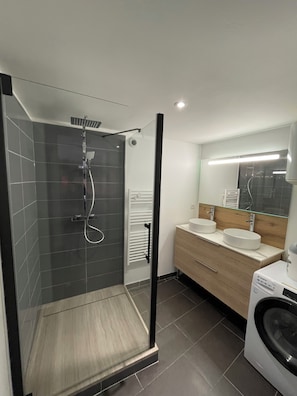 A modern bathroom with a glass-enclosed shower, two sinks, a mirror, and a washing machine.