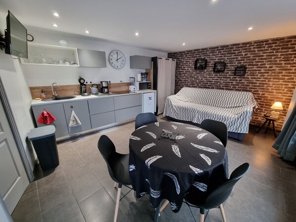 Un espace de vie compact comprenant un coin cuisine, une table à manger, un canapé et un mur en briques.