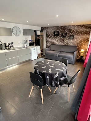 A modern kitchen with a dining area, a grey sofa, and a brick wall.