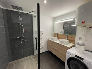 Une salle de bain moderne dotée d’une douche à parois de verre, d’un lave-linge encastré et d’un meuble-lavabo avec deux vasques.