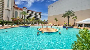 A large outdoor swimming pool surrounded by palm trees and lounge chairs, with a hotel building in the background. - Gulf View Resort Penthouse Condo! Beach & Pools (Panama City Beach)