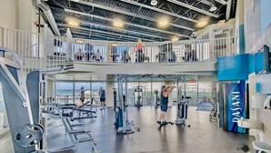 A multi-level gym with various exercise equipment, a mezzanine level with a railing, and a view of the outside. - Gulf View Resort Penthouse Condo! Beach & Pools (Panama City Beach)