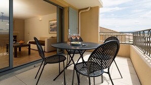A balcony with a round table and four chairs, a bottle of water, and two glasses of wine. - Appart 6p +  balcon/terrasse privée, près du golf (Saumane-de-Vaucluse)