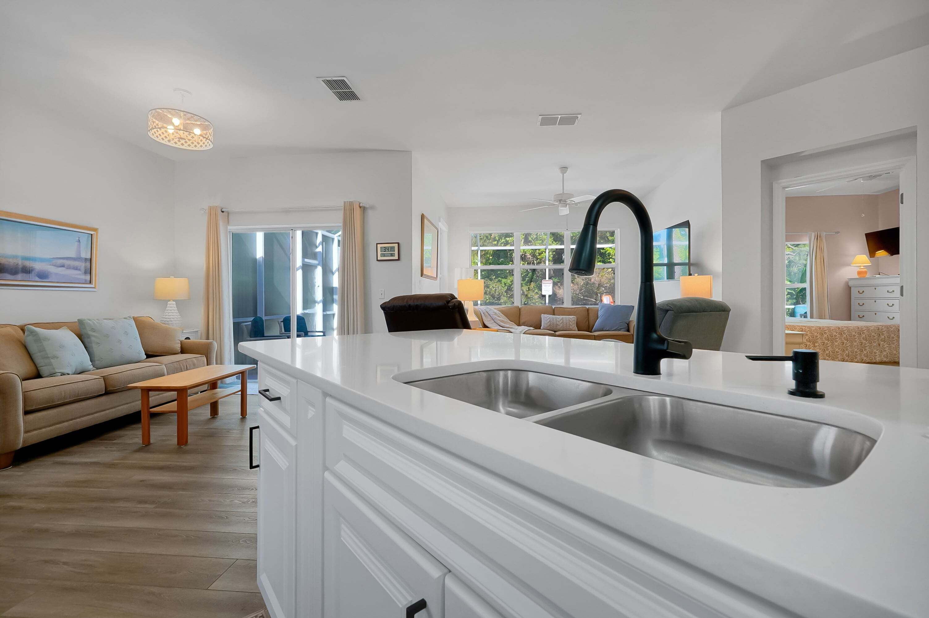 A modern kitchen with a white countertop, double sink, and a dining area with a sofa and table.