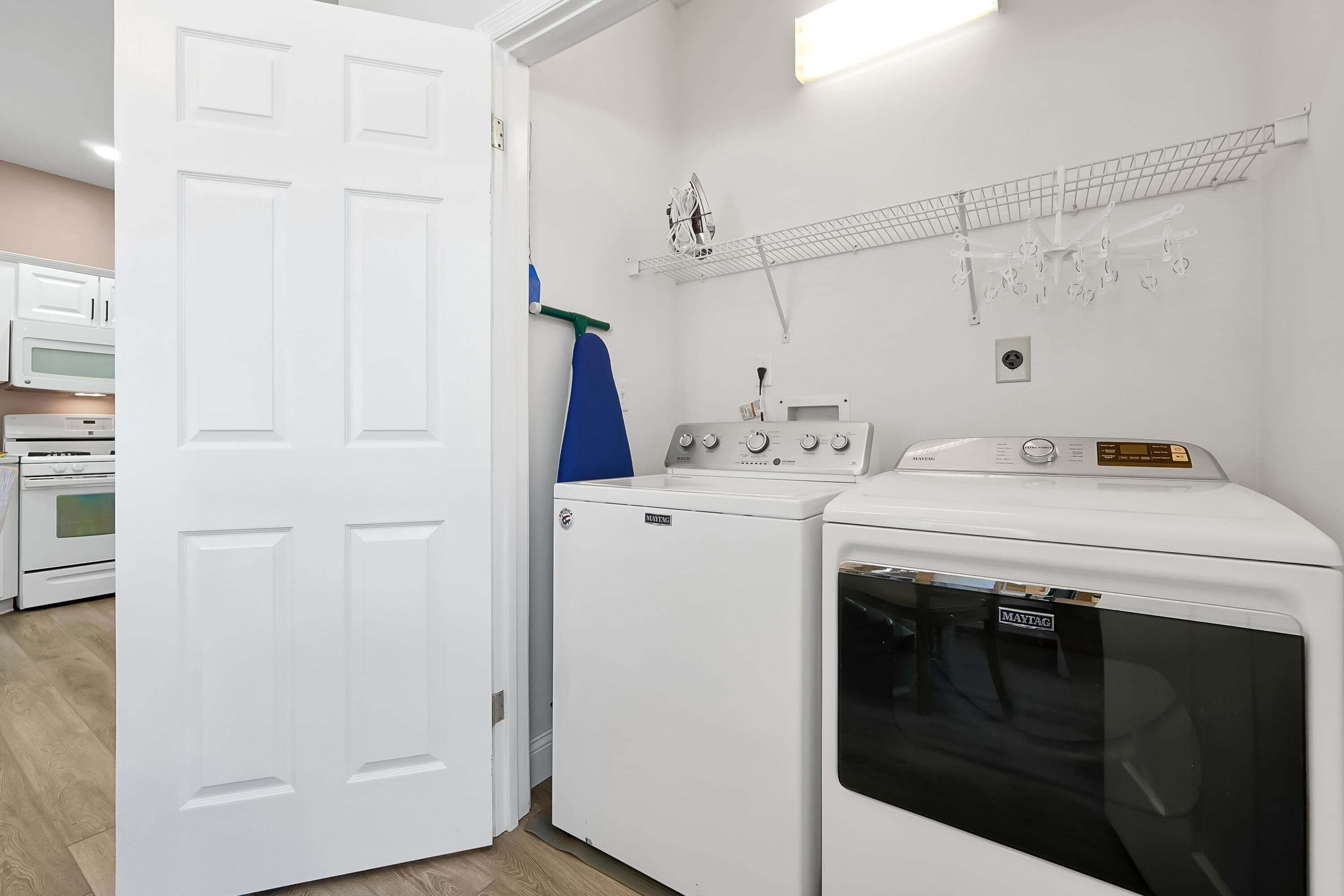 A laundry room with a front-loading washer and dryer, a microwave, and a shelf with hanging items.